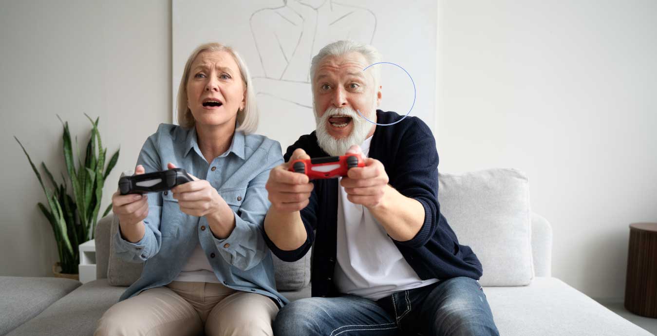 Pareja de personas mayores jugando videojuegos con entusiasmo en un sofá